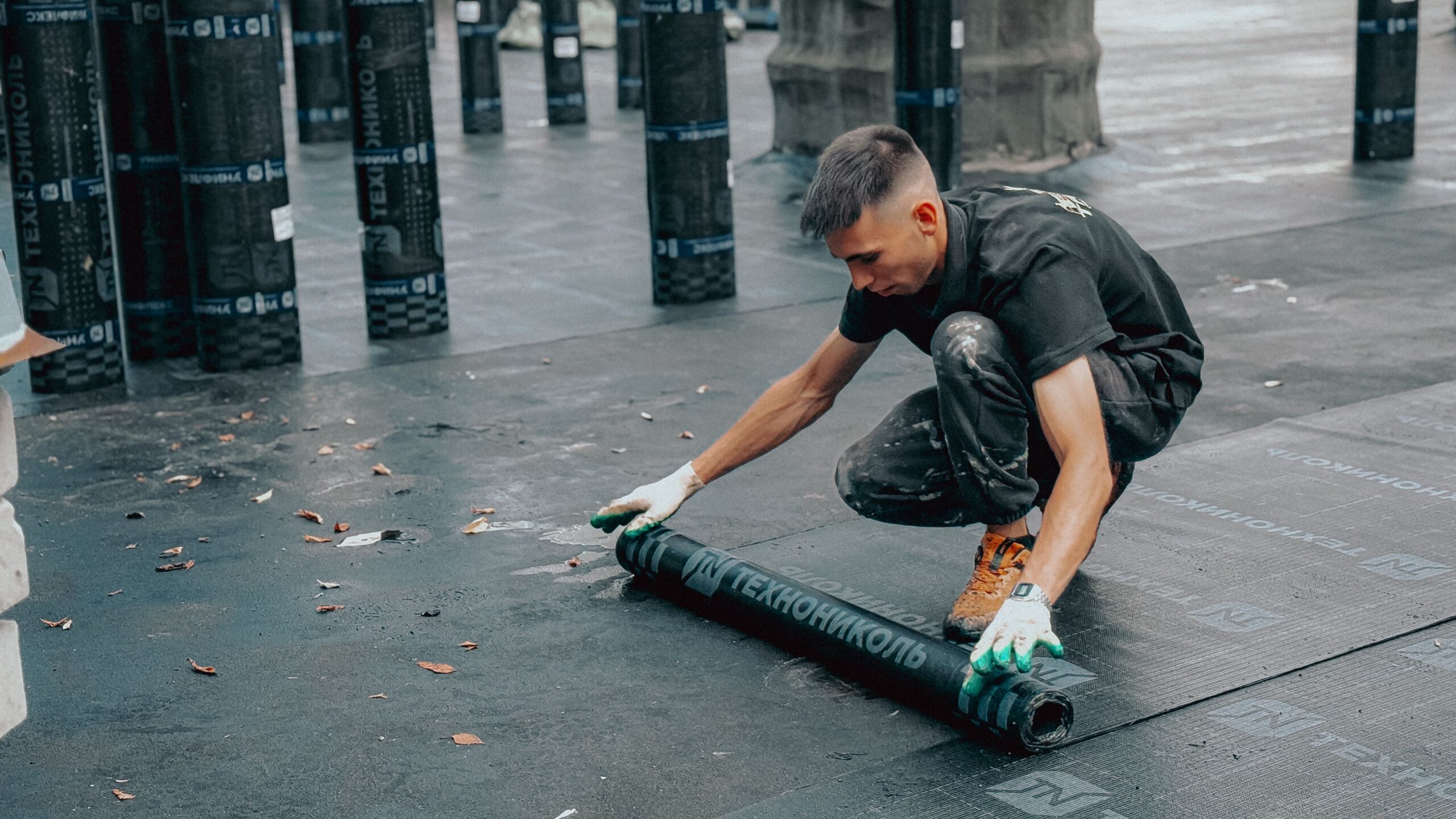 Construction worker applies waterproof membrane on rooftop for protection against weather elements.